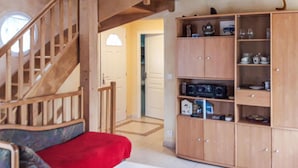 Eine Holztreppe führt zu einer zweiten Etage, ein rotes Sofa mit einem weißen Tisch und eine Holzkommode mit verschiedenen Gegenständen.