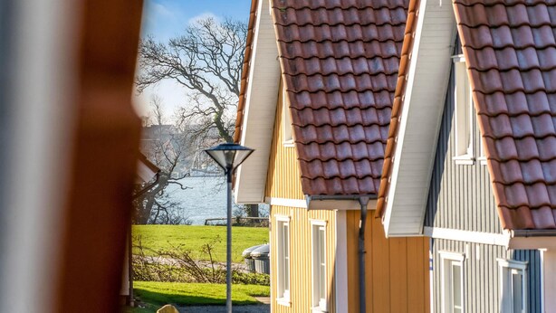 A row of houses with brown tiled roofs, a lamp post, and a grassy area with a body of water in the background. - 4 bedroom lovely home in Gråsten (Gråsten)