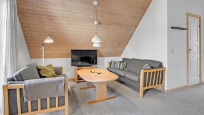 A cozy living room with a wooden ceiling, a flat-screen TV, a grey sofa, a wooden coffee table, and a grey armchair with a blanket. - 4 bedroom lovely home in Gråsten (Gråsten)