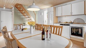 A modern kitchen with white cabinets, a dining table with chairs, a hanging light fixture, and a wooden staircase. - 4 bedroom lovely home in Gråsten (Gråsten)