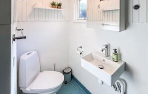 Une petite salle de bain blanche, avec des toilettes, un lavabo et une poubelle.