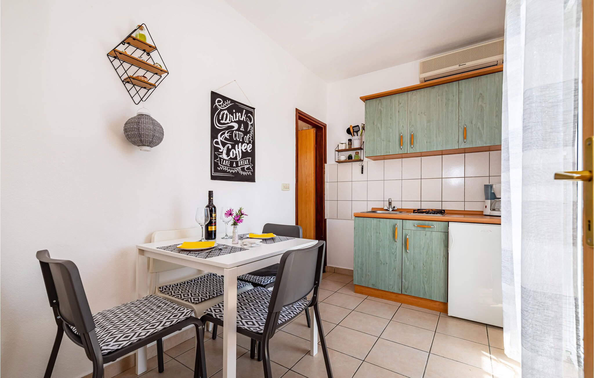 A compact kitchen with green cabinets, a white refrigerator, and a dining area with a table and chairs.