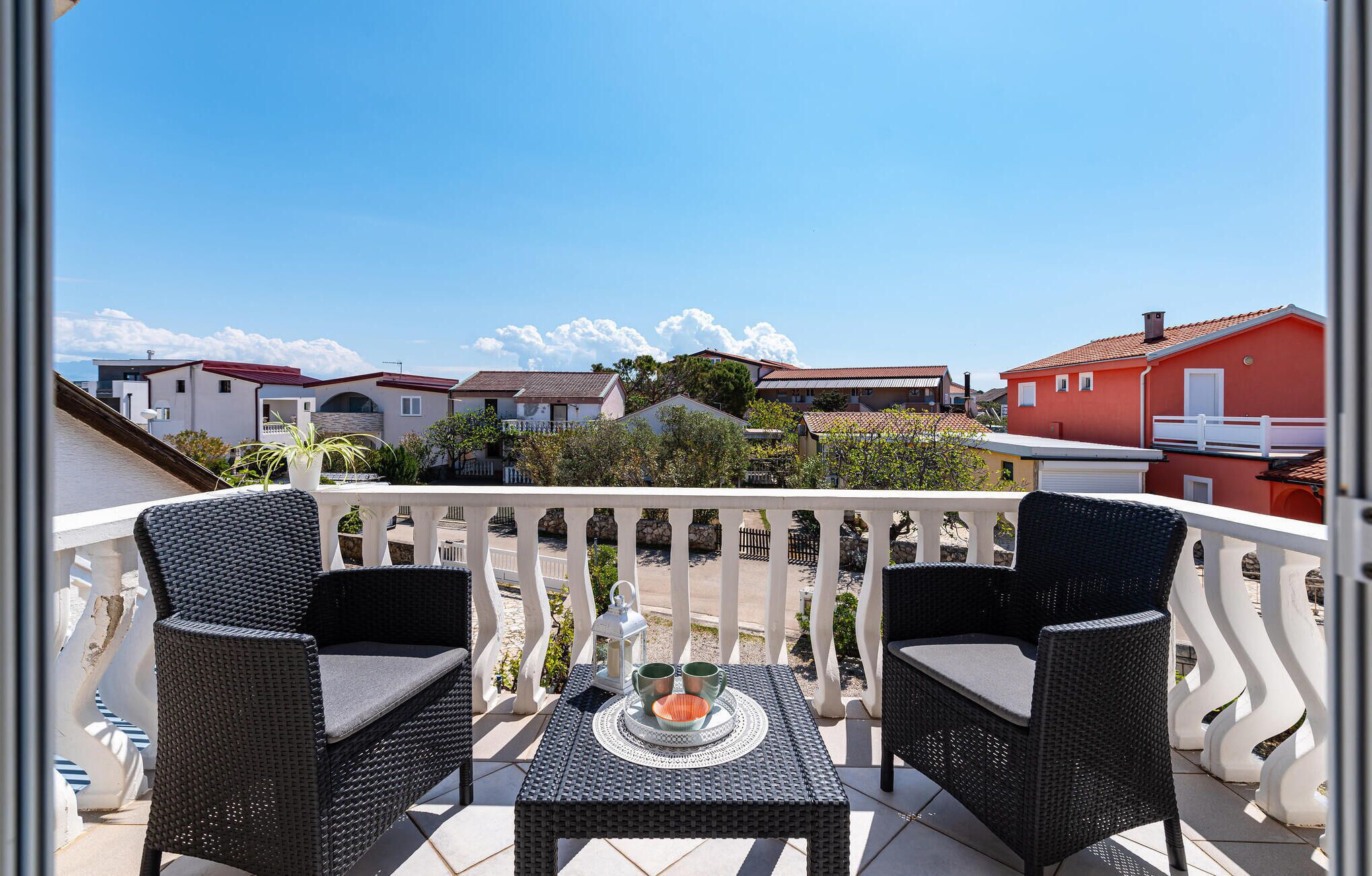 A balcony with wicker furniture, a table with a decorative tray, and a view of neighboring houses.