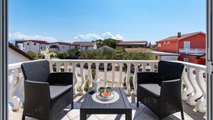 Un balcón con mobiliario de mimbre, una mesa con una bandeja decorativa y vistas a casas vecinas.