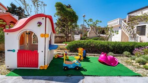Un área de juegos infantiles con una casita, un tobogán y diversos juguetes.