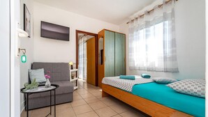 Un dormitorio con cama, una silla, una mesita, un televisor y un armario.