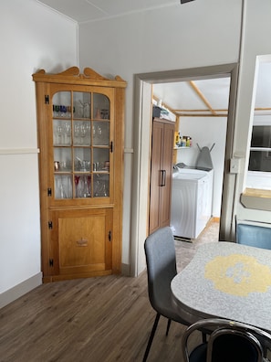 Un comedor con un armario de madera que contiene cristalería, una mesa con mantel estampado y una silla gris.