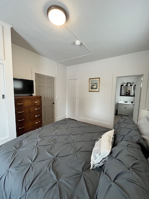 Un dormitorio con cama, cómoda, televisor y puerta que da a un baño.