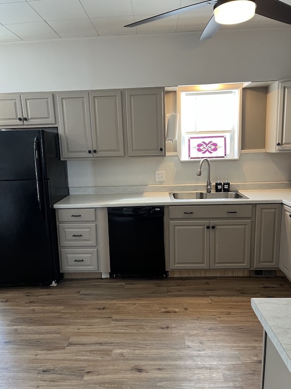 Una cocina con armarios blancos, un refrigerador negro, un lavavajillas y una ventana con azulejos decorativos.