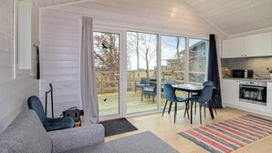 Un salon moderne avec un canapé gris, une table à manger avec des chaises, un coin cuisine équipé d’un four à micro-ondes et une porte-fenêtre coulissante donnant sur une terrasse.