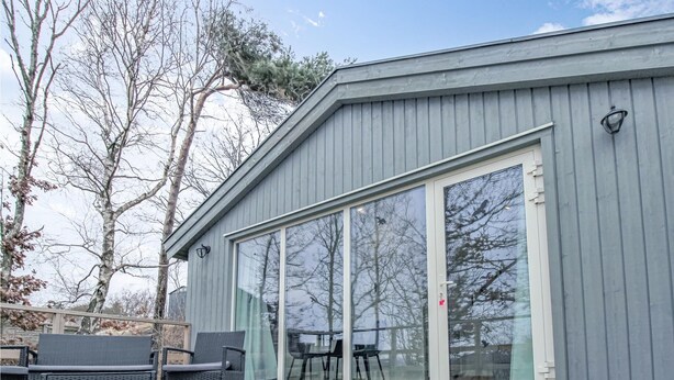 Un bâtiment moderne à l’extérieur gris, doté de grandes portes-fenêtres coulissantes et d’une terrasse aménagée avec du mobilier d’extérieur.