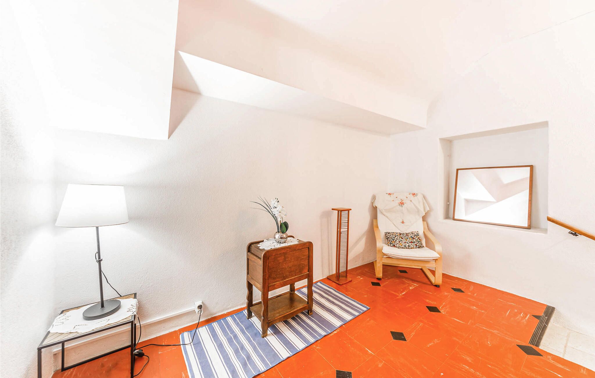 A room with a desk, chair, lamp, and a framed picture on the wall.