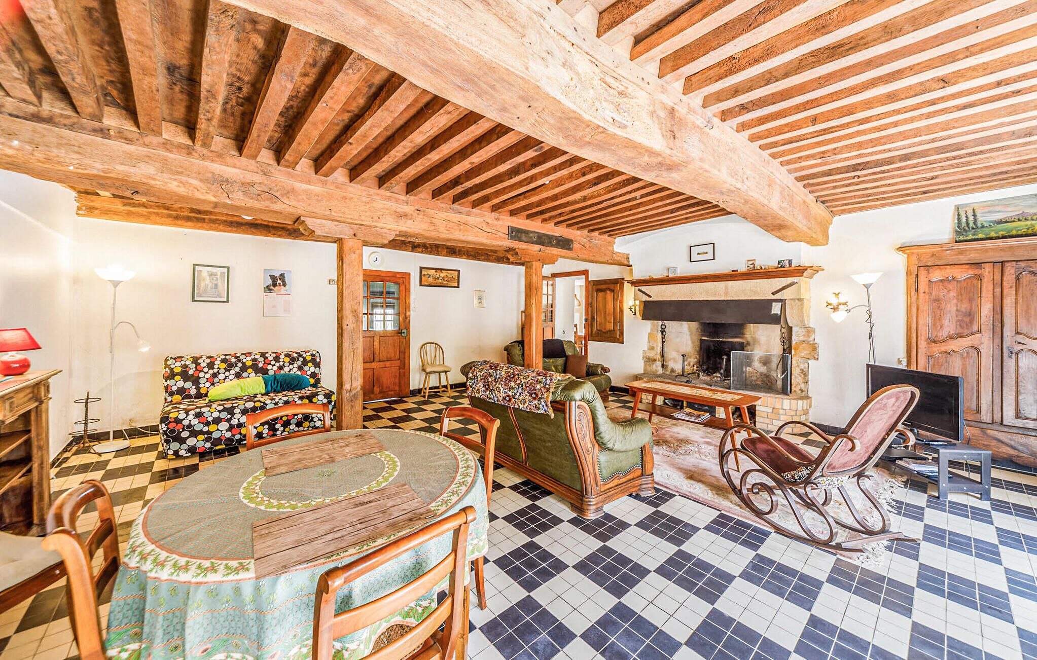 Un salón rústico con vigas de madera a la vista, suelo de cuadros, chimenea y muebles tradicionales.