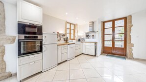 Eine moderne Küche mit weißen Schränken, einem Backofen, einem Kühlschrank und einem großen Fenster.