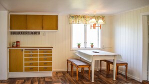 Une cuisine compacte avec des meubles en bois, une table à manger avec des bancs et une fenêtre agrémentée de rideaux à motifs floraux.