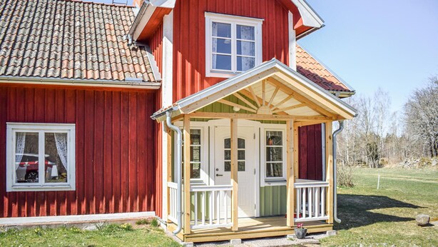 Une maison rouge à deux étages, dotée d’un porche en bois et d’un toit recouvert de tuiles.