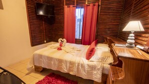 A bedroom with a bed, a wooden nightstand, a red rug, a TV mounted on the wall, and red curtains. - Cabaña SantaClara your best choice (La Fortuna)