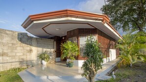 A modern house with a flat roof, a concrete wall, and a small garden with potted plants and a palm tree. - Cabaña SantaClara your best choice (La Fortuna)