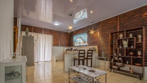 A modern kitchen with wooden paneling, a dining area with chairs, a white cabinet with glass doors, and a television mounted on the wall. - Cabaña SantaClara your best choice (La Fortuna)