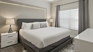 Moderni hotellihuone, jossa on suuri sänky, yöpöydät valaisimineen, työpöytä ja ikkuna, jossa on sälekaihtimet.