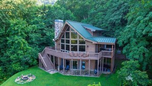 Une grande cabane en bois à deux étages, dotée d’une terrasse périphérique et entourée d’une forêt dense.