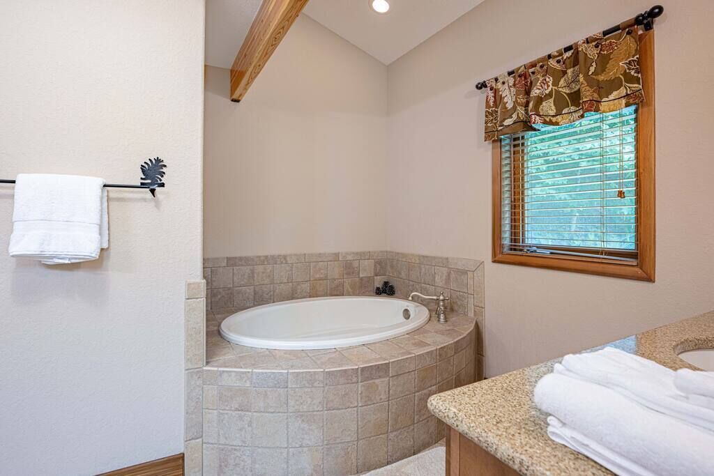 A bathroom with a freestanding bathtub, a vanity with a sink, and a window with blinds.