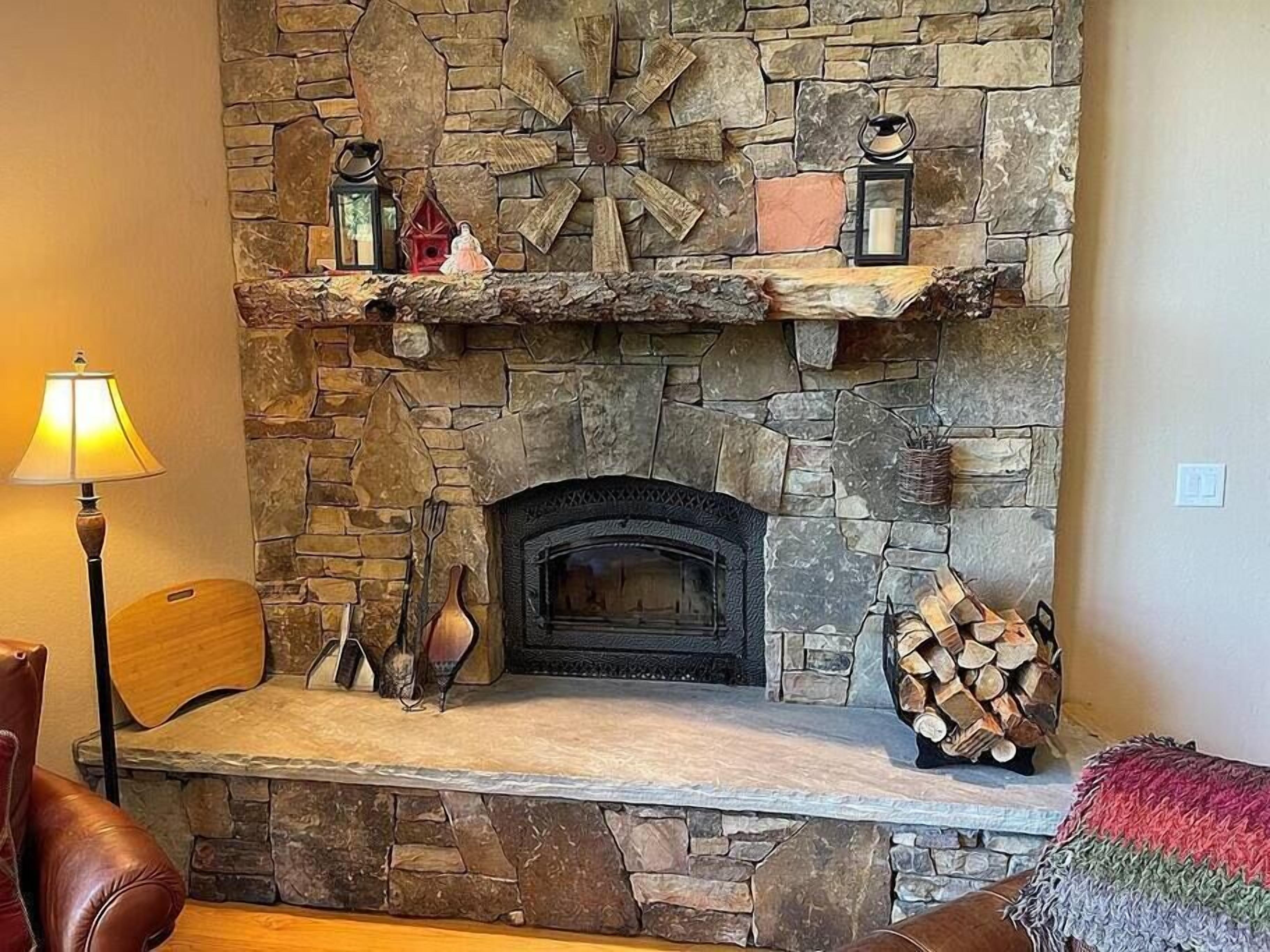 Una chimenea de piedra con repisa, leña apilada y una lámpara.