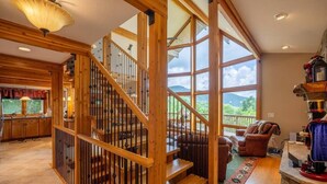 Un vaste espace de vie agrémenté d’un escalier en bois, d’une grande fenêtre offrant une vue sur l’extérieur et d’un coin salon confortable avec une cheminée.
