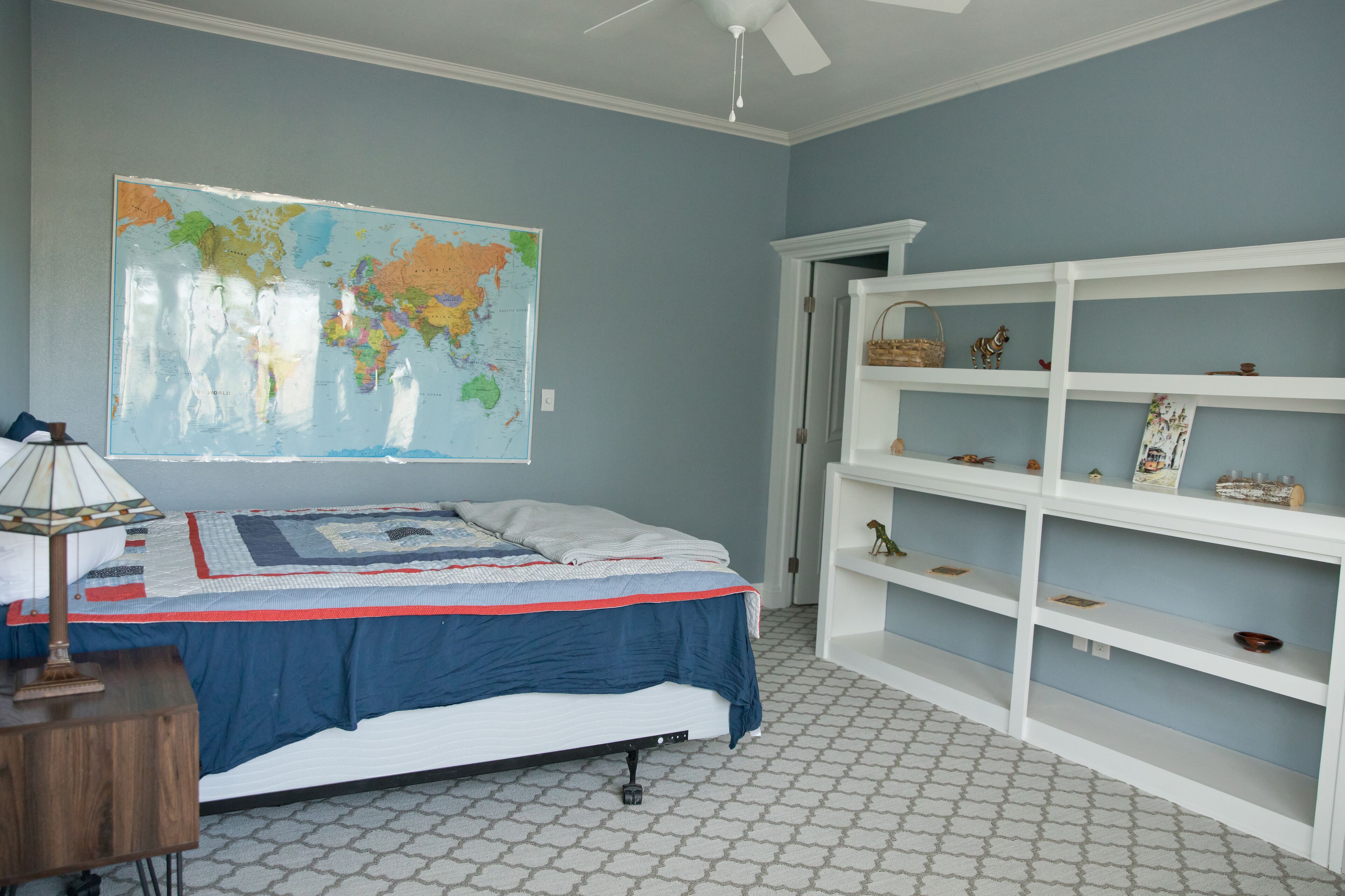 Une chambre à coucher avec un lit, une carte accrochée au mur, une bibliothèque et un sol à motifs.