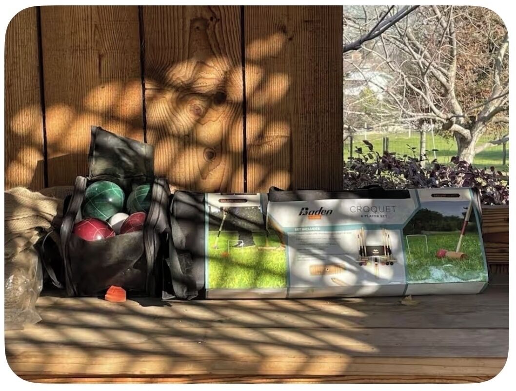 Ein Croquet-Set und Kugeln auf einer Holzterrasse, im Hintergrund ein Holzbau.