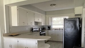 Una cocina moderna con armarios blancos, un refrigerador negro y un comedor con mesa y sillas blancas.
