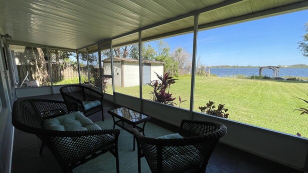 Un patio cubierto con muebles de mimbre y vistas a un lago.