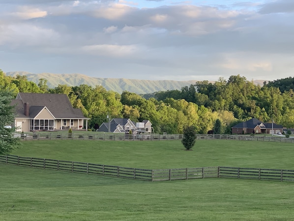 A rural landscape with houses, a fenced field, and mountains in the background.