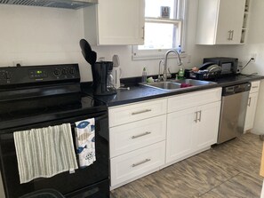 Una cocina con armarios blancos, estufa negra, un lavamanos y lavavajillas.