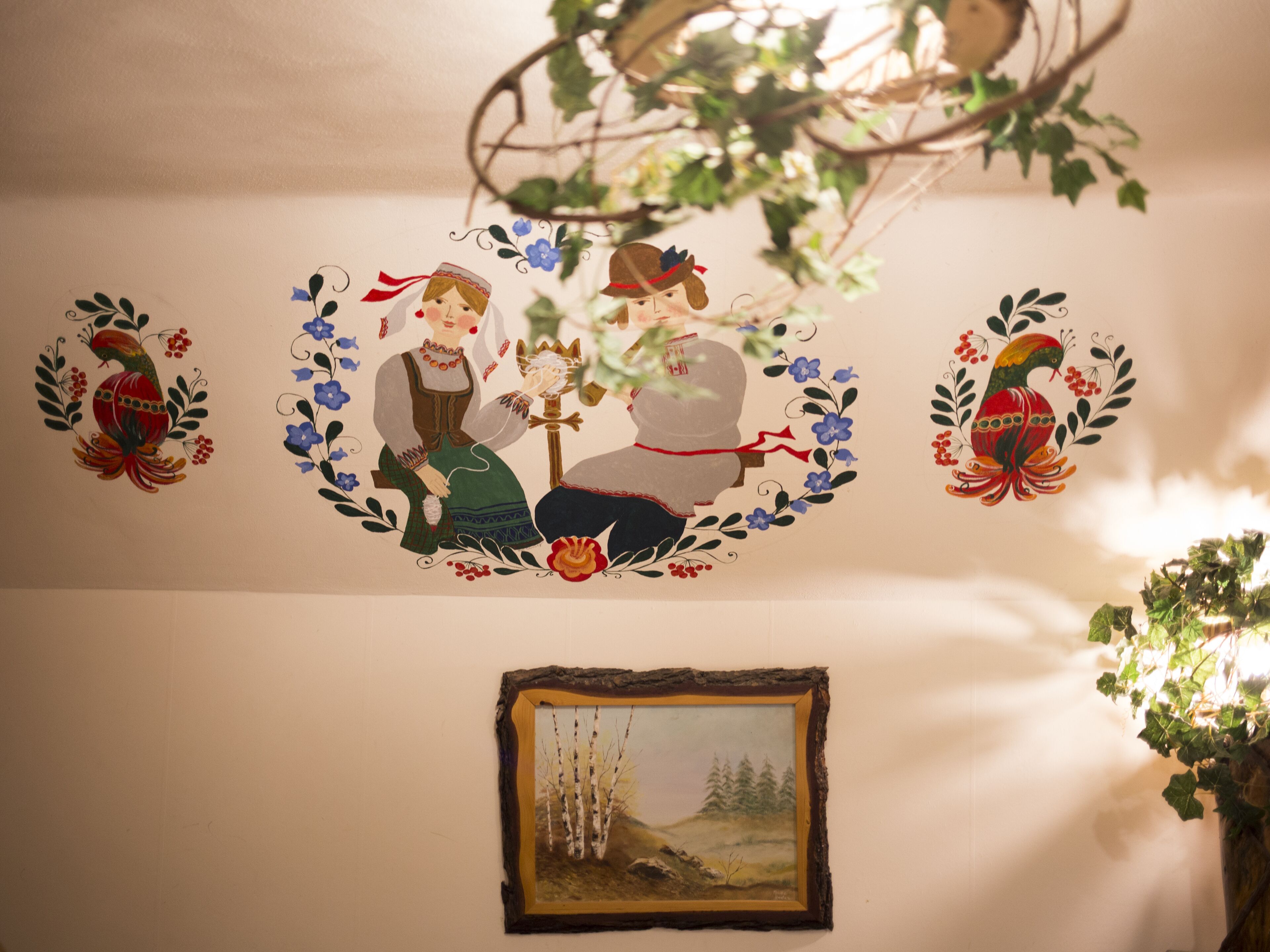 Een muur met traditionele volkskunst decoraties, een lijst met een landschapschilderij, en een hangende plant.