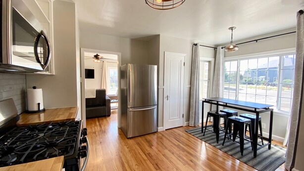 A modern kitchen with a stainless steel refrigerator, a stove, and a dining area with a table and chairs. - Lavish Luxury in a Lush Locale (Cheyenne)