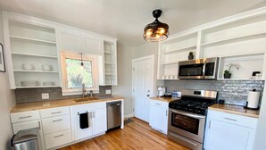 A modern kitchen with white cabinetry, a stainless steel stove, and a wooden countertop. - Lavish Luxury in a Lush Locale (Cheyenne)