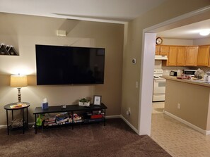 A living room with a flat-screen TV, a small table with a lamp, and a shelf with board games.