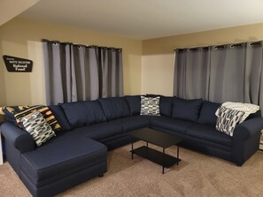 A living room with a dark blue sectional sofa, a small black coffee table, and grey curtains.