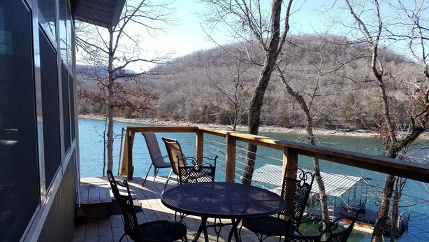 A wooden deck with a table and chairs overlooking a lake, surrounded by trees and a dock. - Hoot Owl Cabins -Incredible Lakefront Cabin PLUS a 2nd Tiny Home (Garfield)