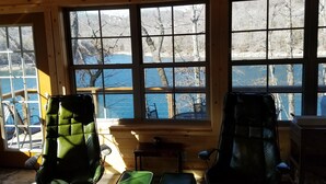 A cabin interior with large windows, wooden walls, and two green leather chairs. - Hoot Owl Cabins -Incredible Lakefront Cabin PLUS a 2nd Tiny Home (Garfield)