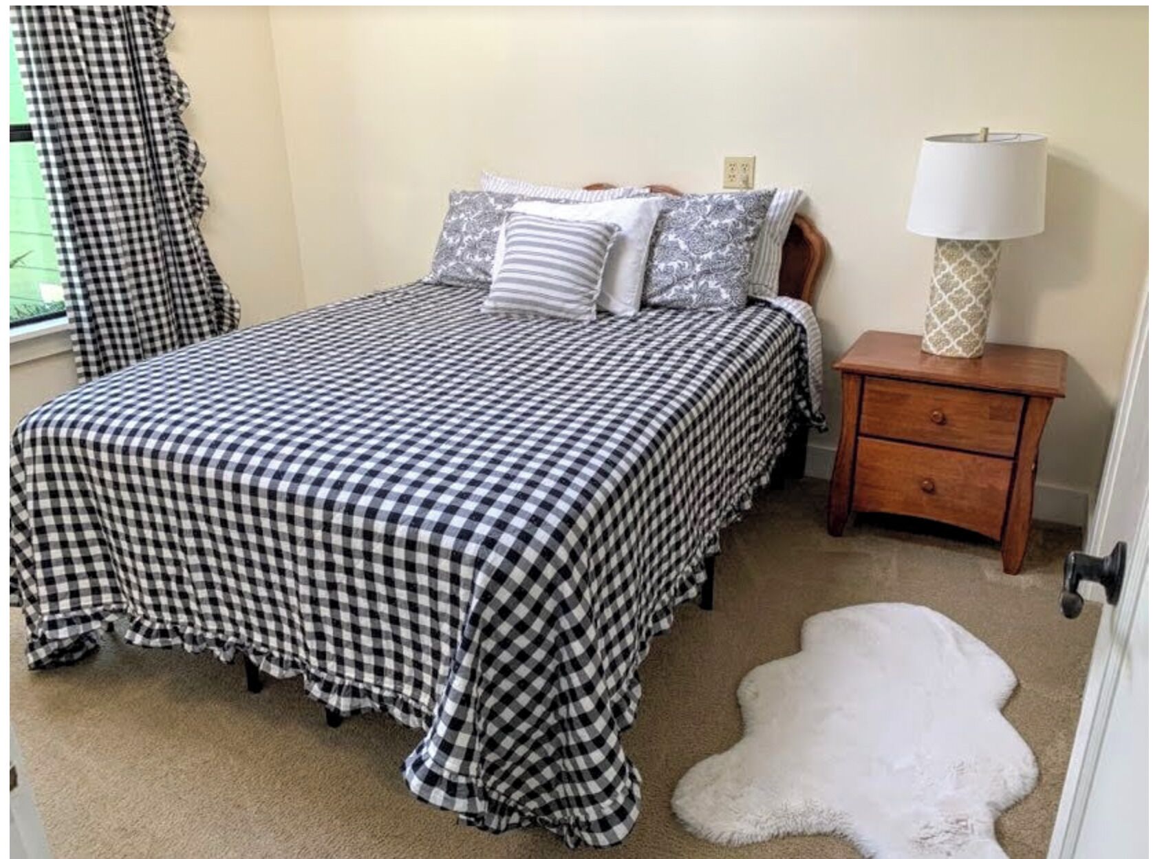 A bedroom with a checkered bedspread, a nightstand with a lamp, and a white furry rug.