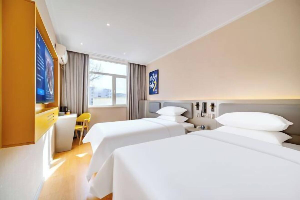 A hotel room with two beds, a desk, a chair, a TV, and a window with curtains.