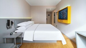 A modern hotel room with a neatly made bed, a bedside table with a lamp, and a wall-mounted phone.