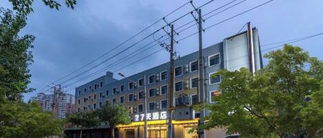 A multi-story hotel with a modern facade, a visible restaurant or cafe on the ground floor, and a parking area in front.