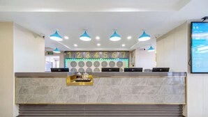 A hotel reception area with a marble counter, blue pendant lights, and a digital clock displaying the time.