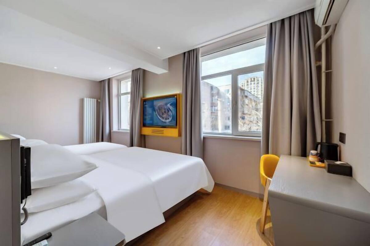 A hotel room with a bed, a desk, a chair, a TV, and a window with curtains.