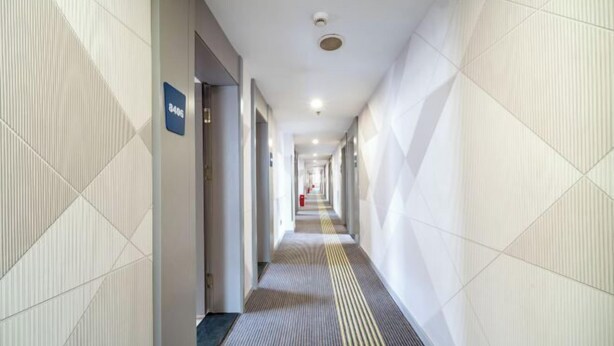 A long, narrow hallway with a patterned floor and walls, a sign indicating room number 8406, and a fire extinguisher visible in the distance.