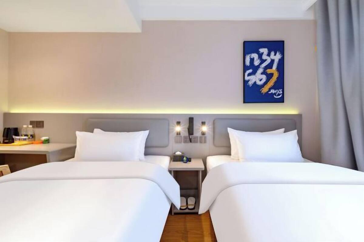 A hotel room with two beds, a nightstand, a mirror, and a wall-mounted artwork.