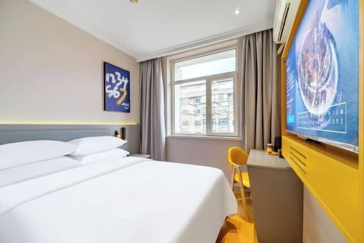 A hotel room with a bed, a TV, a window, and a chair.